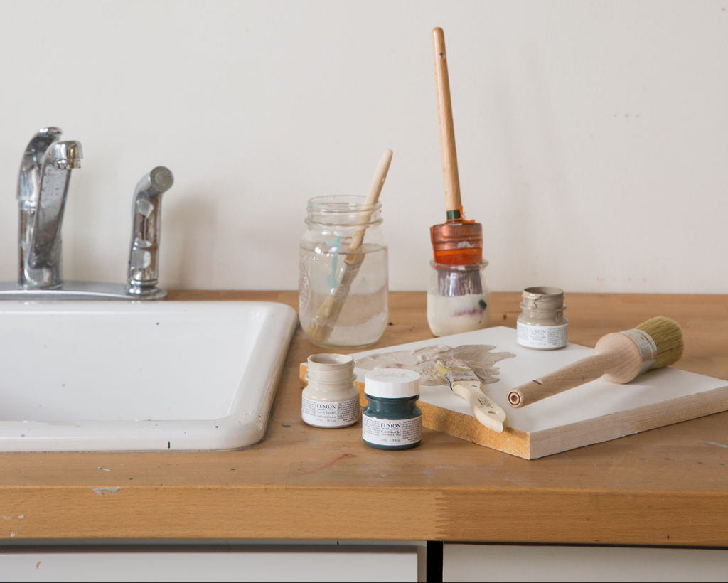 Art supplies on a wooden table next to a sink with a shelf above